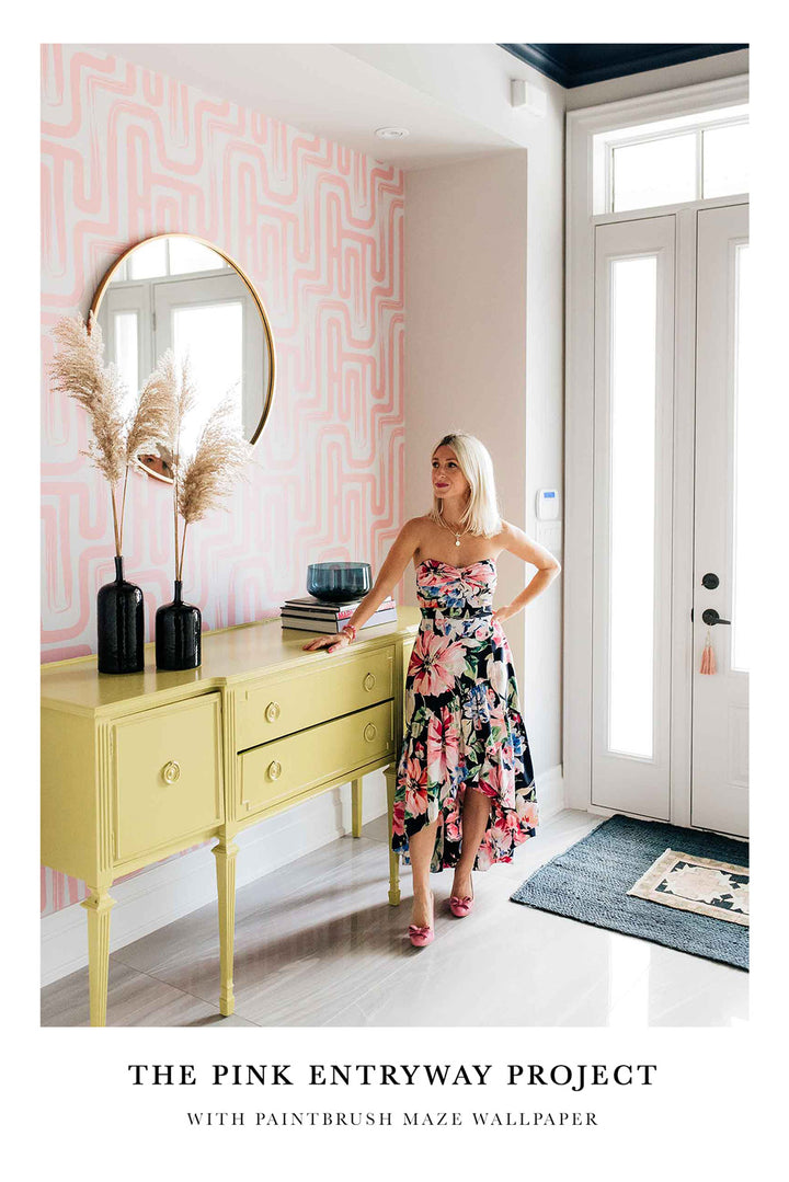 Bold and eclectic entryway interior with light pink removable wallpaper, yellow vanity, round mirror and pampas grass decor